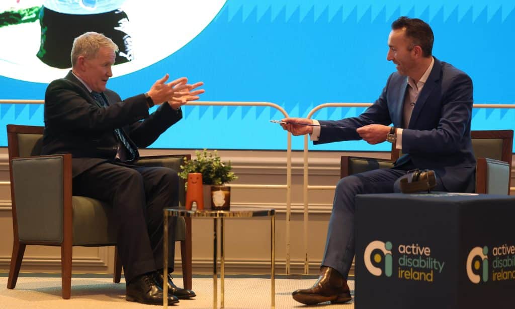 Rob Hartnett sitting across from Munro Ruigrok on a stage as Minro shows his Dublin City Marathon medal
